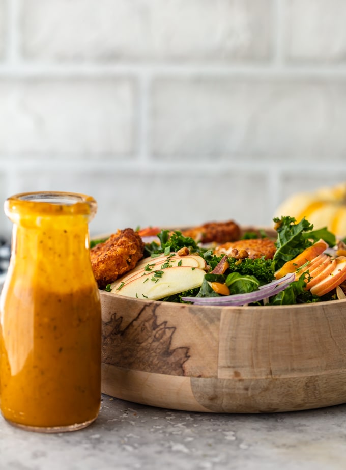 Wooden salad bowl filled with kale salad, next to a jar of maple pumpkin kale salad dressing