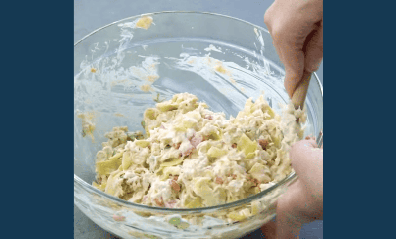 A person mixing a refreshing salad with crab and artichoke dip in a bowl.