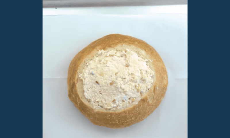 A loaf of bread stuffed with tuna salad and topped with a crab artichoke dip.