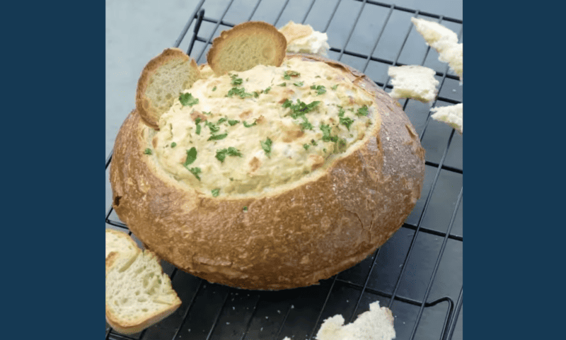 A delicious crab and artichoke dip served in a bread bowl with melted cheese and bread on top.