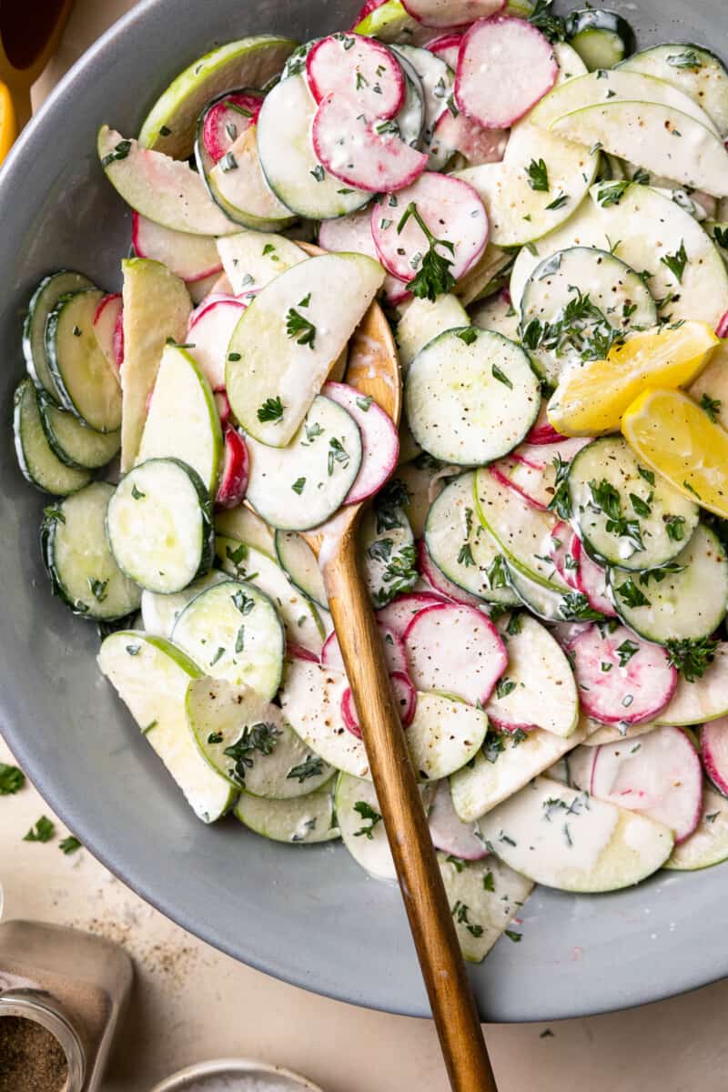 creamy cucumber salad in a gray serving bowl with wooden salad serving utensils.