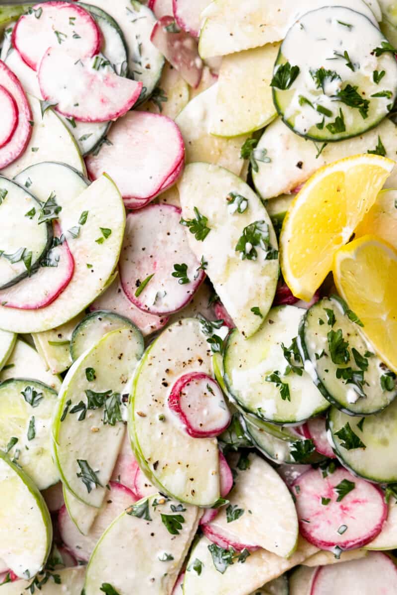 close up of creamy cucumber salad with lemon wedges.