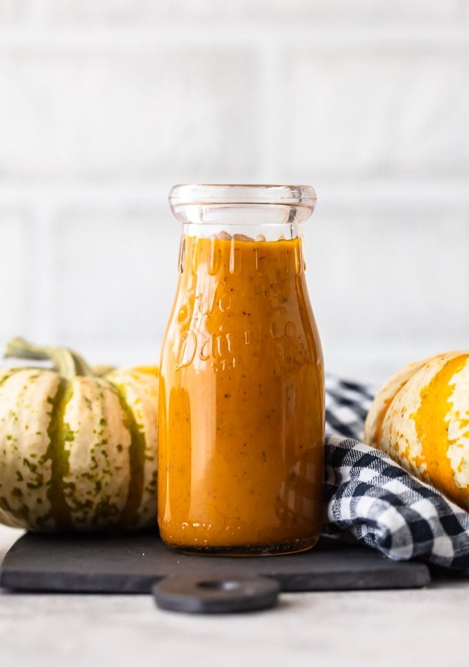 A jar of maple pumpkin kale salad dressing next to mini pumpkins