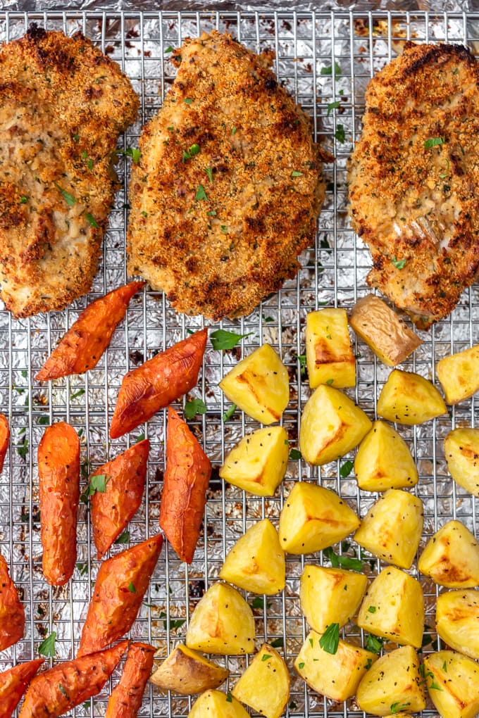breaded baked pork chops on a baking sheet with carrots and potatoes