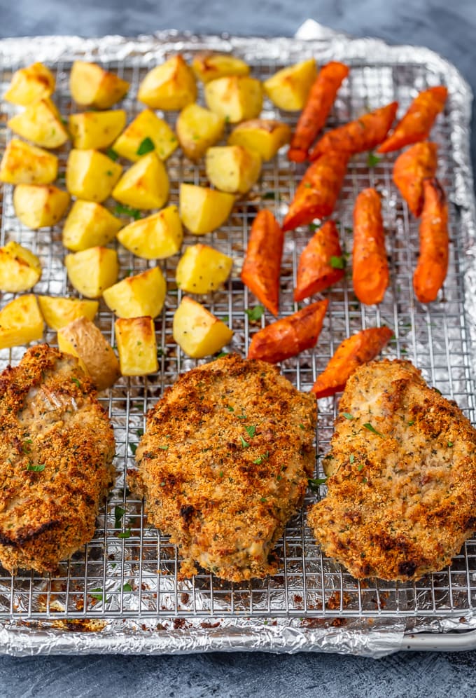 breaded pork chops on a baking sheet with roasted veggies