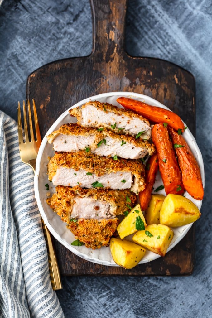 plate of baked pork chops with carrots and potatoes, sitting on a wood cutting board
