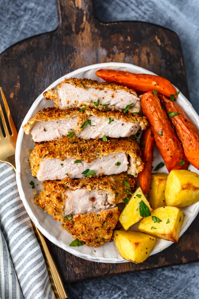 a plate of breaded baked pork chops cut into pieces, with roasted carrots and potatoes
