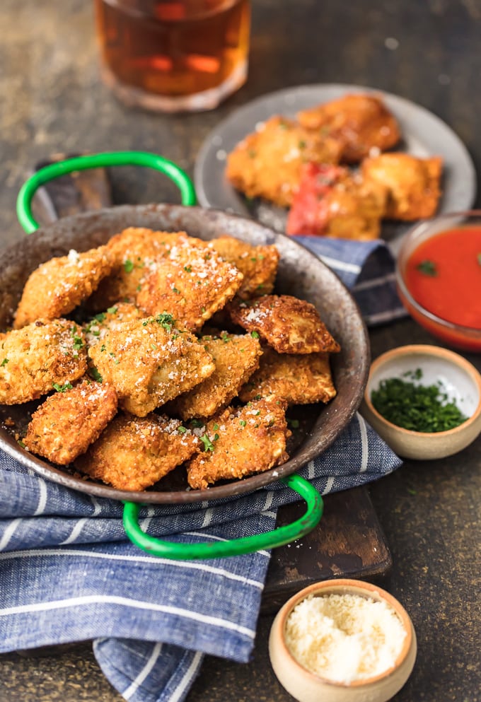 fried ravioli in a pan, next to a plate of raviolis and a bowl of sauce