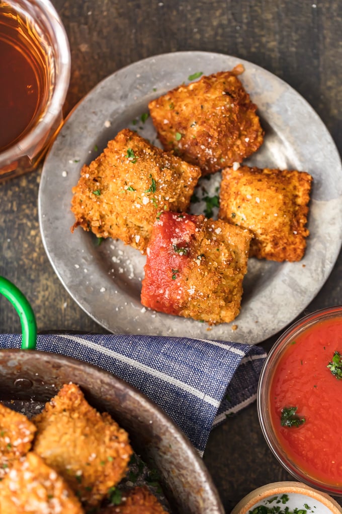 overhead view of toasted ravioli on a small plate, one dipped in marinara sauce