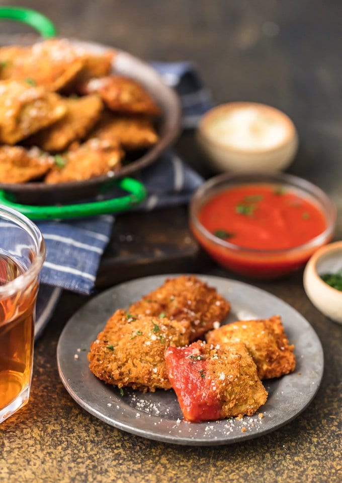 a plate of toasted ravioli in the foreground, a larger plate of ravioli in the background