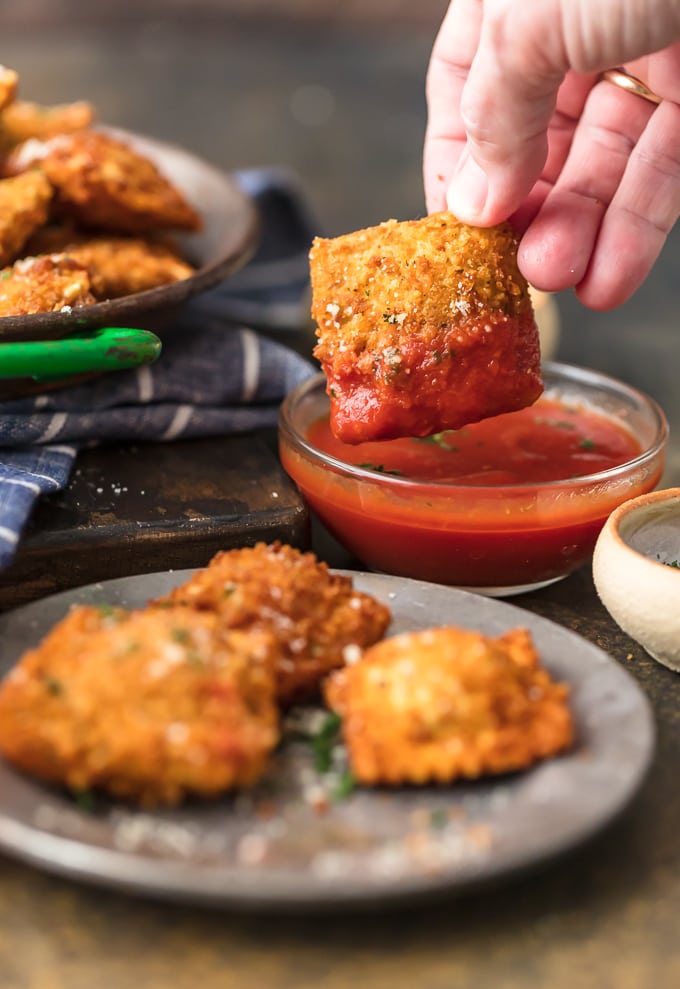 a hand dipping a fried ravioli into marinara sauce.