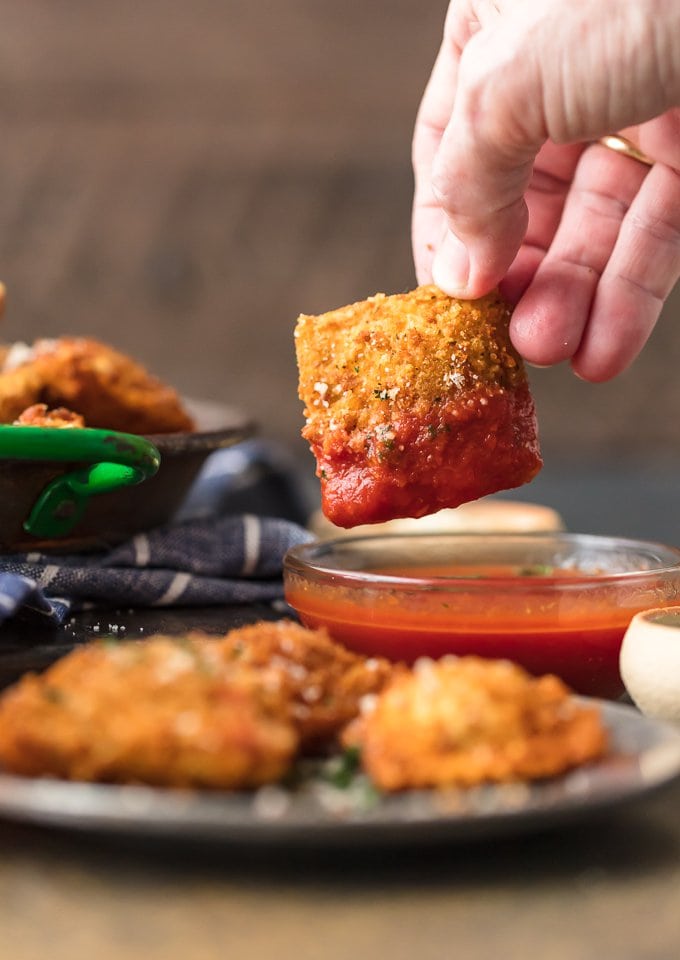 dipping a fried ravioli into a bowl of marinara sauce