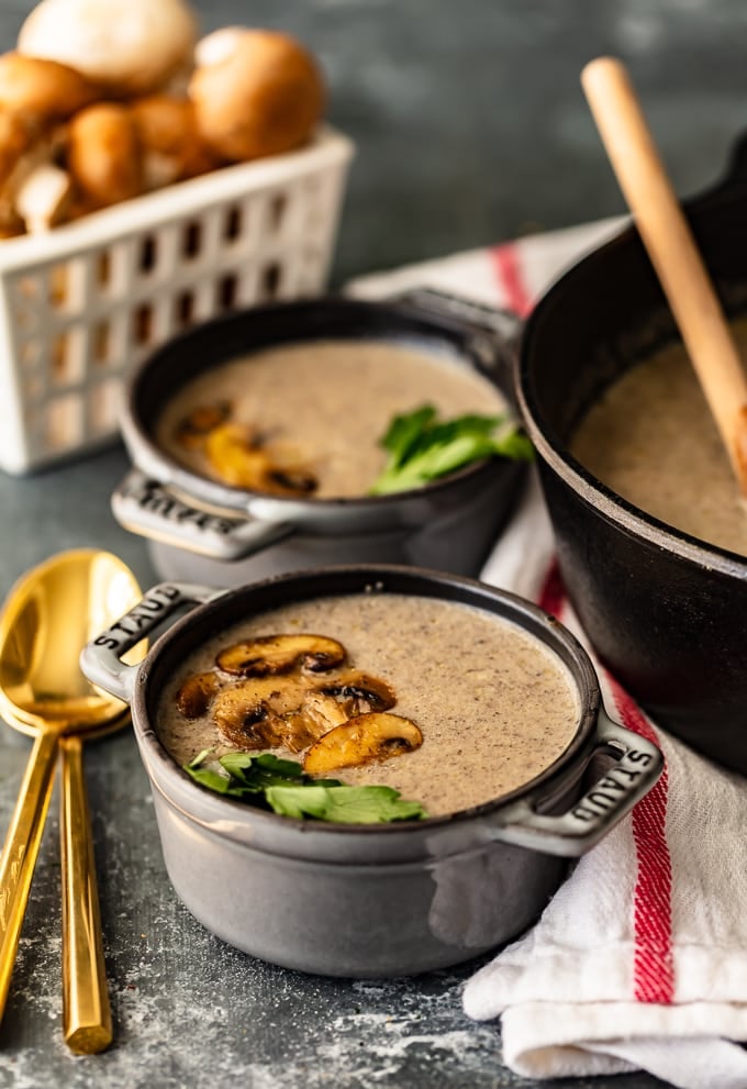 Two bowls of cream of mushroom soup next to a large pot of soup and a basket of mushrooms