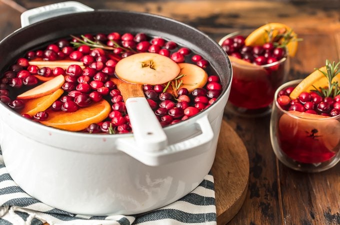 Cranberry hot cider recipe in a large white pot, next to to glasses of cider