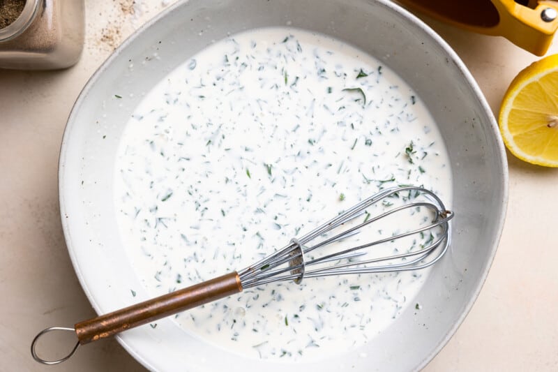 dressing for creamy cucumber salad in a white bowl with a whisk.
