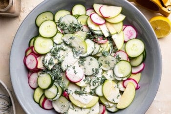dressing and herbs poured on top of creamy cucumber salad.