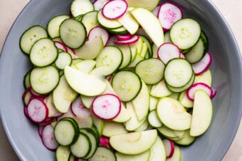 cucumber, radish, and apple slices mixed together in a gray bowl.