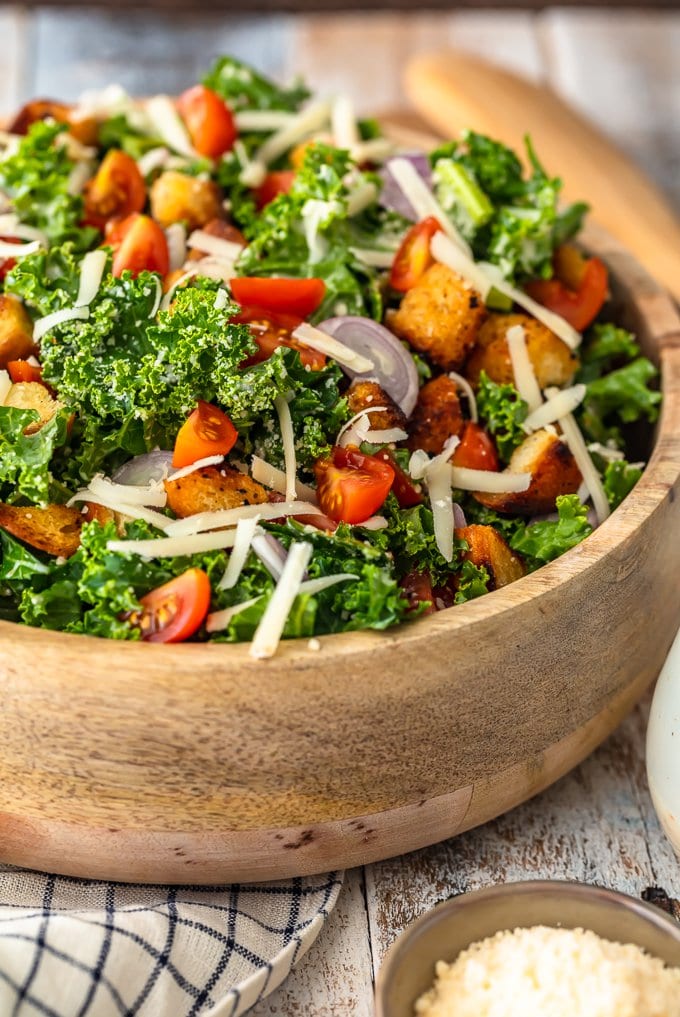 A bowl of kale caesar salad topped with cheese, croutons, tomatoes, and shallots