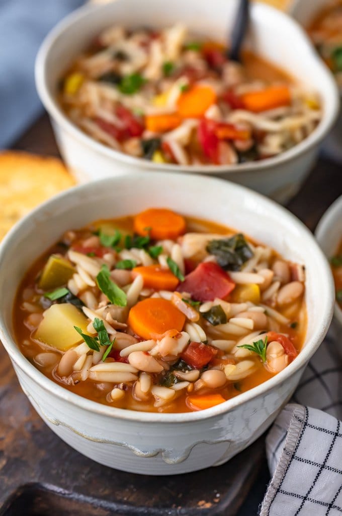 Two bowls of minestrone soup filled with orzo, carrots, beans, and more