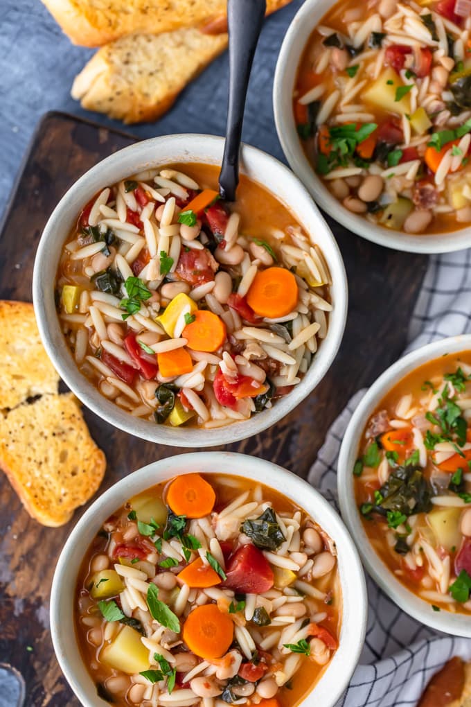Four bowls of minestrone soup on a wooden cutting board