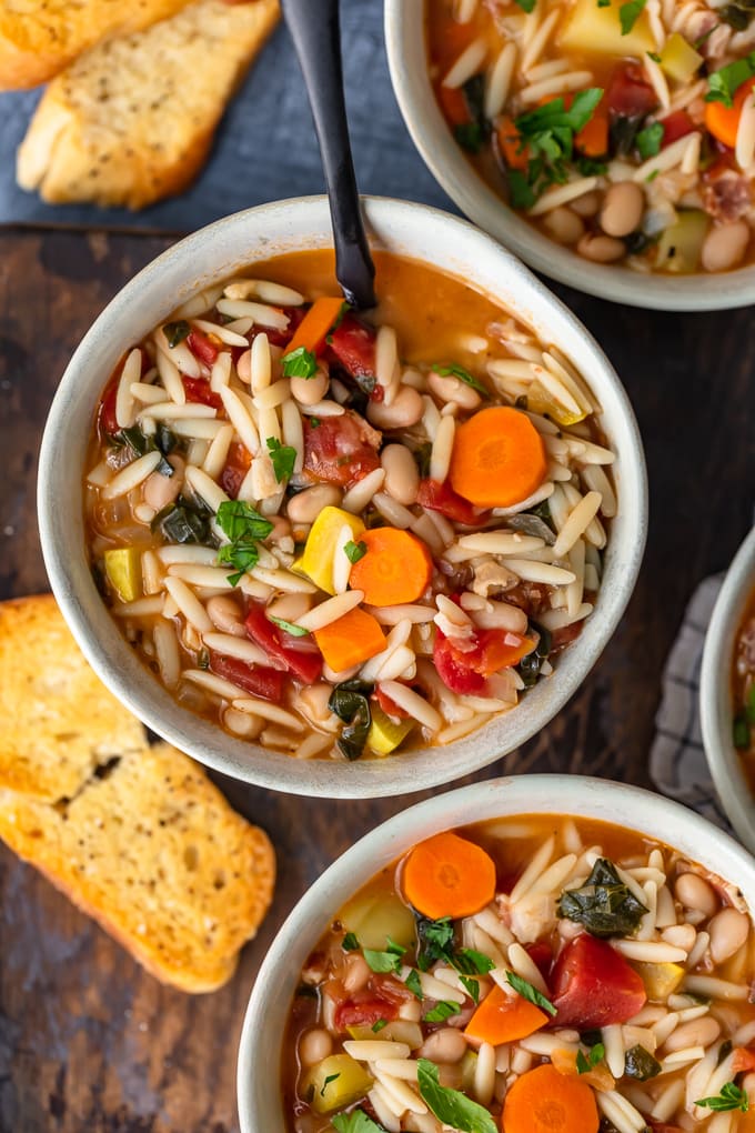 Hearty minestrone soup in white bowls, surrounded by toasted bread