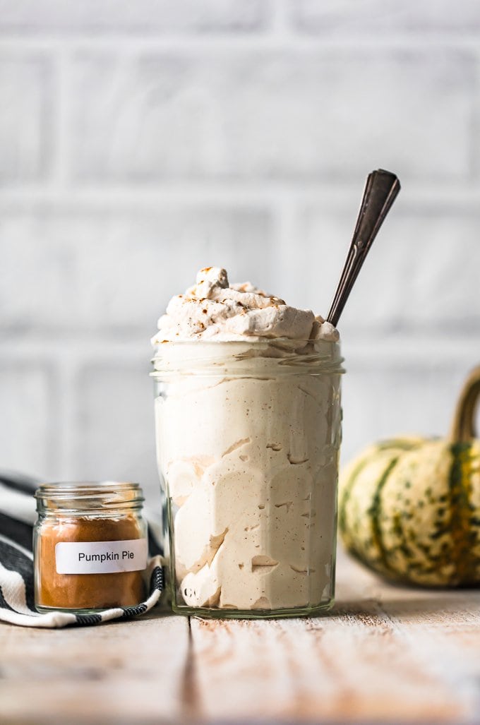 A jar of pumpkin flavored whipped cream, next to a small jar of pumpkin pie spice