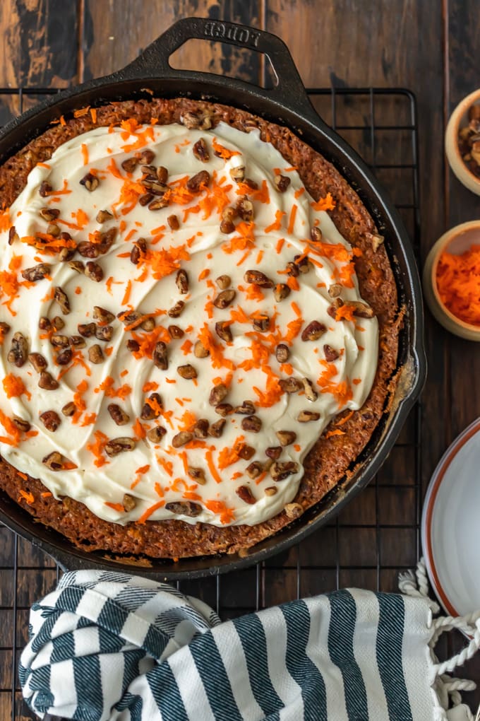 Carrot cake in a skillet, topped with the best cream cheese frosting, pecans, and carrot shavings