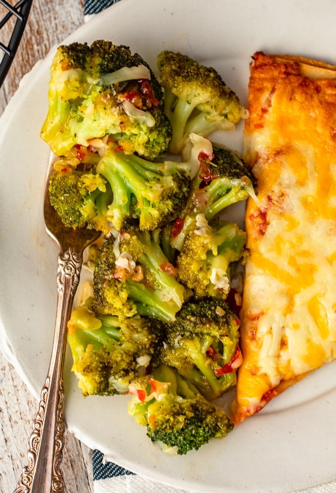 close up view of spicy cheesy broccoli and a slice of cheese pizza on a plate