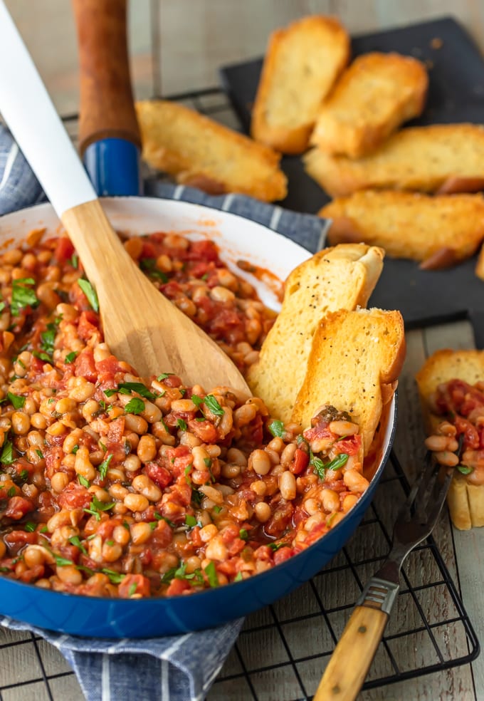 a skillet filled with white bean and tomatoes, with two slices of bread