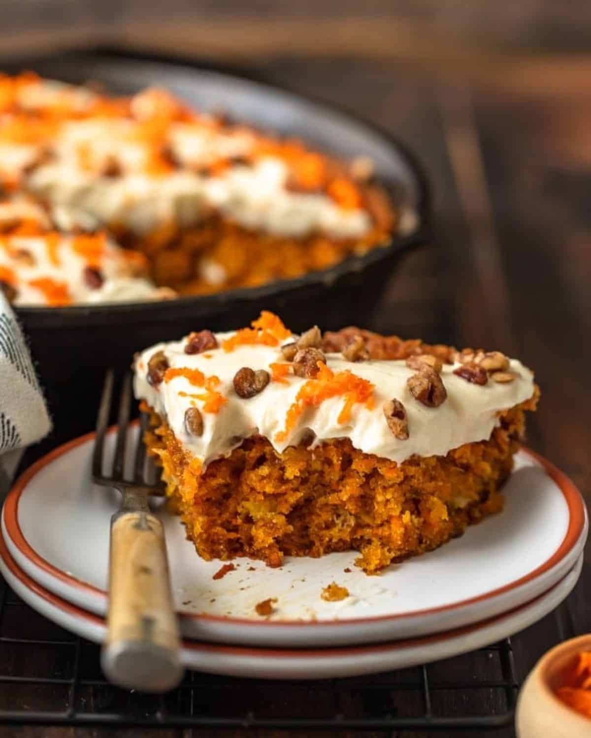 Skillet Carrot Cake is the perfect way to make this delicious dessert without an oven. This easy carrot cake recipe with pineapple is so moist, so flavorful, and so simple! And we're topping it off with the absolute best cream cheese frosting for carrot cake, because it wouldn't be complete without it! A slice of skillet carrot cake on a plate with a fork.