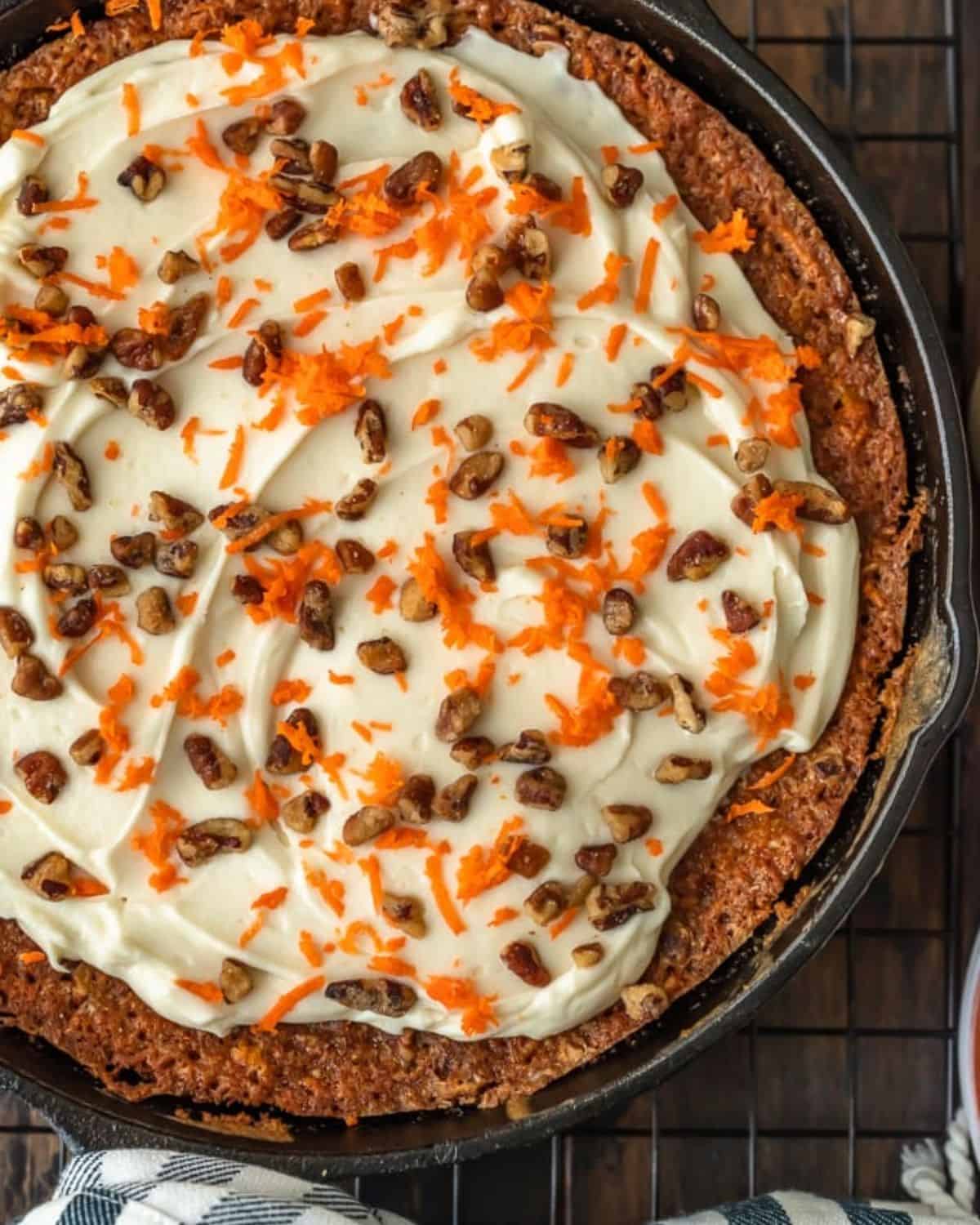 Skillet Carrot Cake is the perfect way to make this delicious dessert without an oven. This easy carrot cake recipe with pineapple is so moist, so flavorful, and so simple! And we're topping it off with the absolute best cream cheese frosting for carrot cake, because it wouldn't be complete without it! Skillet carrot cake with frosting, garnished with shredded carrots and chopped pecans.