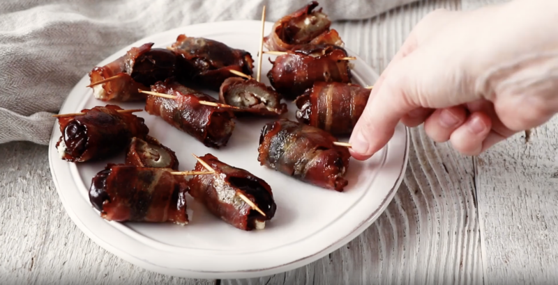 bacon wrapped dates on a white plate.