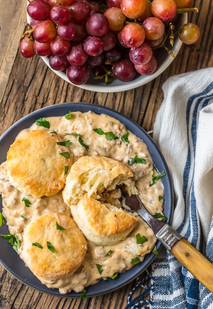 overhead view of a plate of sausage gravy and biscuits next to a bowl of grapes