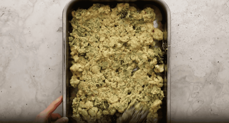 A person is holding a baking pan full of broccoli and cauliflower, preparing a delicious broccoli cauliflower casserole.