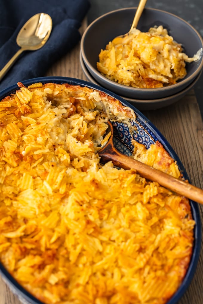 cheesy potato casserole in a blue casserole dish next to a bowl of cheesy potatoes