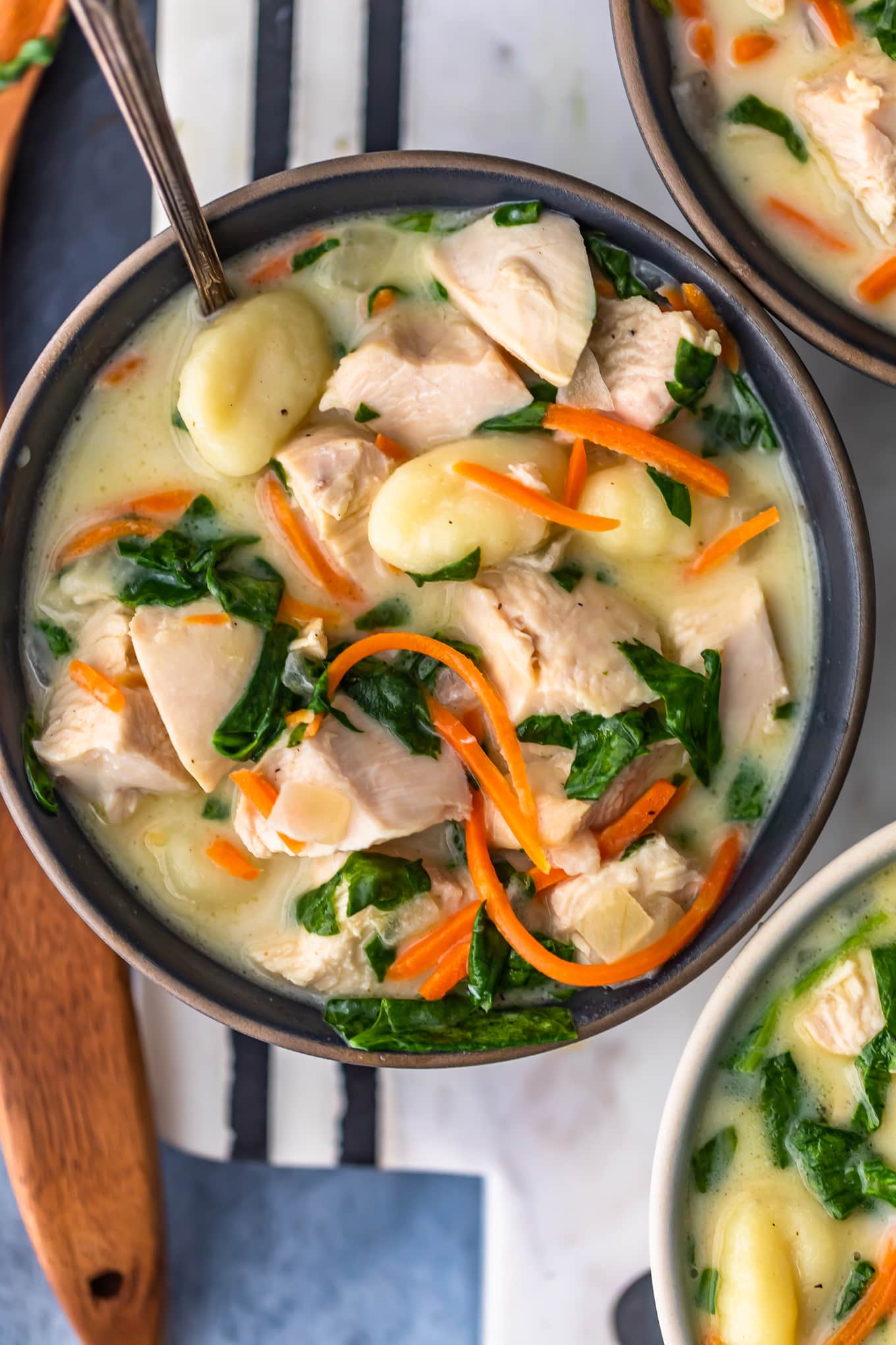 a bowl of creamy soup filled with carrots, gnocchi, chicken, and spinach