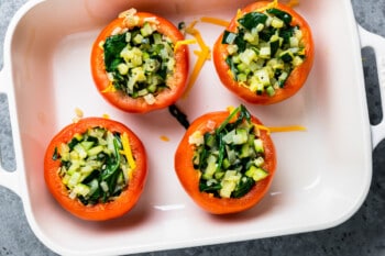 4 tomatoes stuffed with veggie filling in a baking pan.