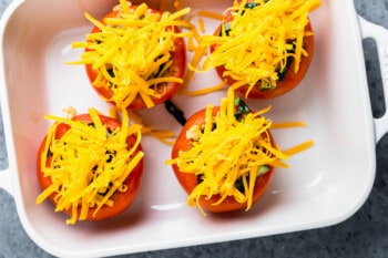 4 stuffed tomatoes in a baking pan topped with cheese.