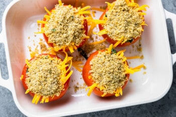 4 stuffed tomatoes in a baking pan topped with cheese and breadcrumbs.
