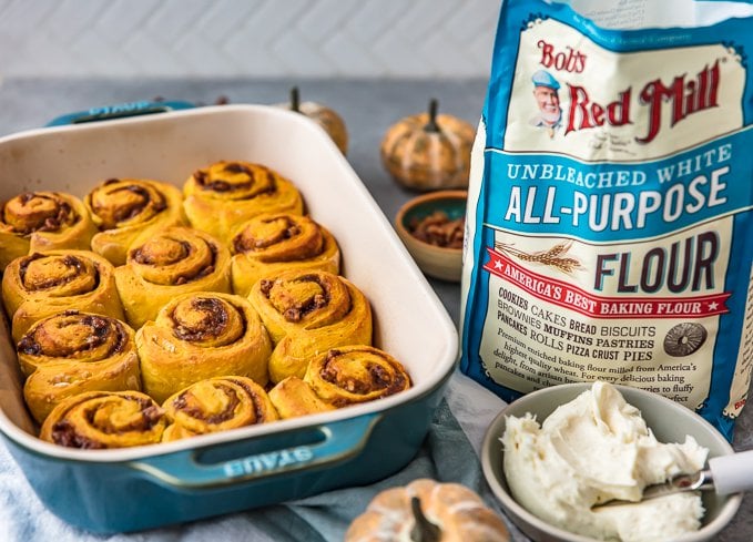 pumpkin cinnamon rolls in a baking dish, next to a bag of flour