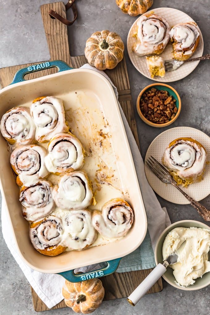 pumpkin cinnamon rolls in a baking dish, next to plates of cinnamon rolls