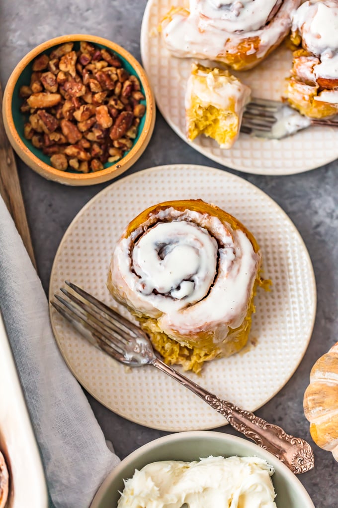 overhead view of cinnamon rolls on a white plate, next to a small bowl of pecans