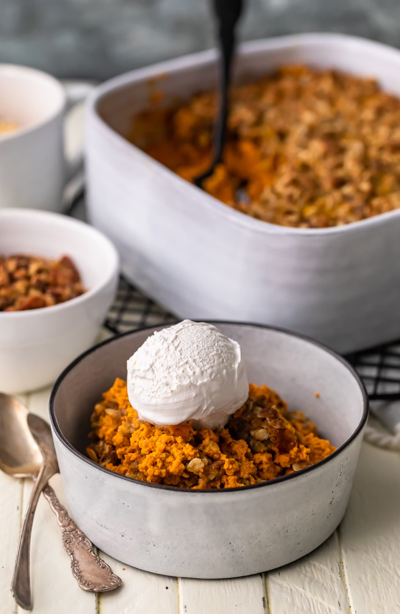 white bowl filled with pumpkin crumble recipe in the foreground, a baking dish filled with crumble dessert in the background