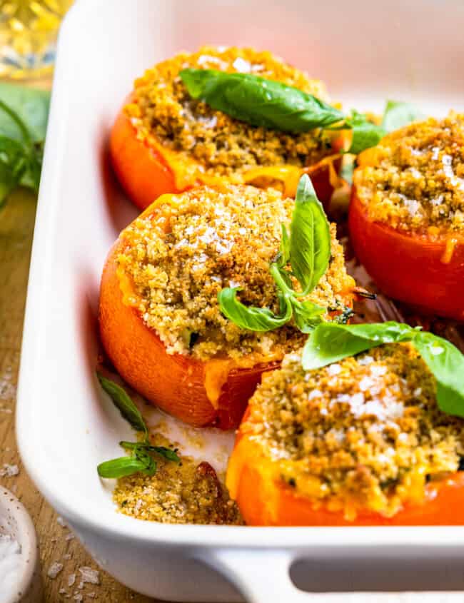 three-quarters view of 4 stuffed tomatoes in a white baking pan.