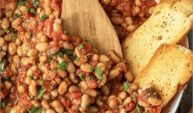 A pan full of white beans in tomato sauce, being stirred with a wooden spoon.