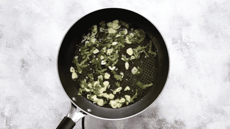 Fried garlic in a frying pan with white beans in tomato sauce.