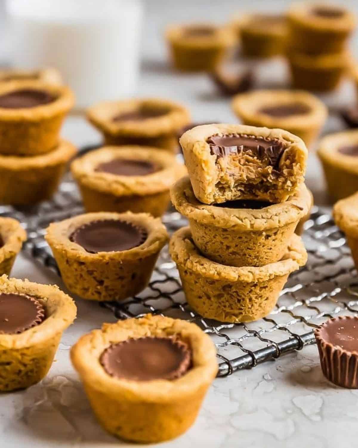 Peanut Butter Cup Cookies are the perfect little treat. Mini peanut butter cups are baked right into tart shaped cookies for a delicious bite-sized dessert. Everyone will eat these Reese's Cup Cookies right up because no one can resist chocolate peanut butter cookies! Peanut butter cup cookies stacked with one with a bite taken out of it.