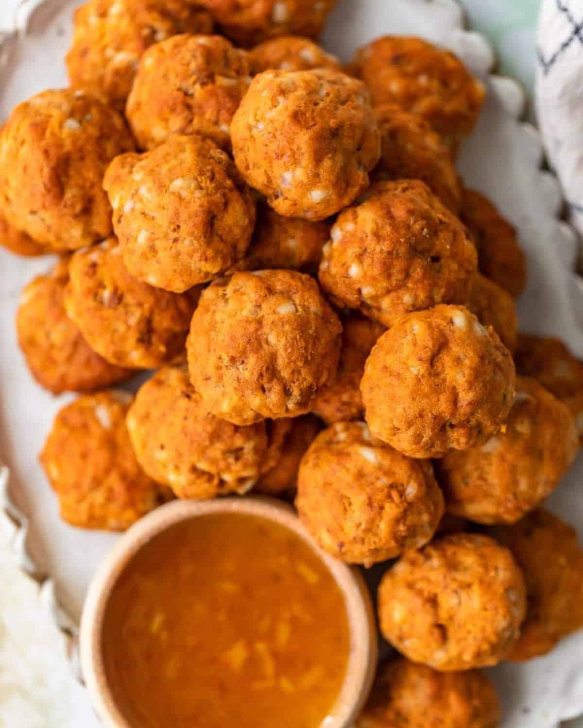 This Sausage Cheese Balls recipe puts a sweet and spicy twist on a classic appetizer. These easy sausage balls are made with cheese, sweet potato, and chorizo, and they taste amazing! Dip these Sweet Potato Sausage Balls in a spicy marmalade sauce for the final touch. Sweet potato chorizo cheese balls on a platter with marmalade sauce.