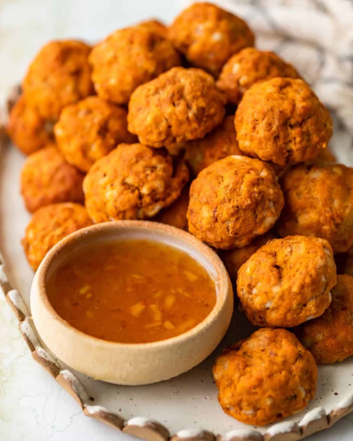 This Sausage Cheese Balls recipe puts a sweet and spicy twist on a classic appetizer. These easy sausage balls are made with cheese, sweet potato, and chorizo, and they taste amazing! Dip these Sweet Potato Sausage Balls in a spicy marmalade sauce for the final touch. Sweet potato chorizo sausage cheese balls on a platter with marmalade sauce.
