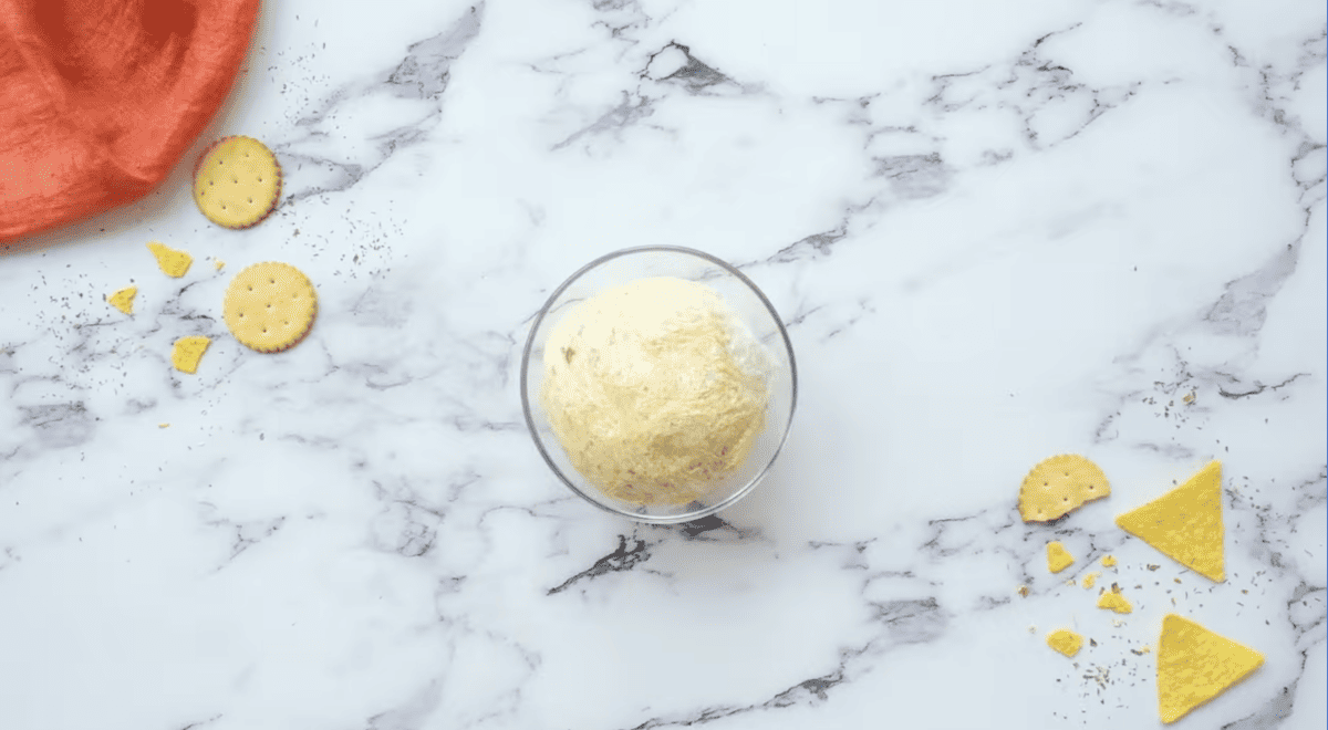 a shaped cheese ball wrapped in plastic wrap in a small glass bowl.